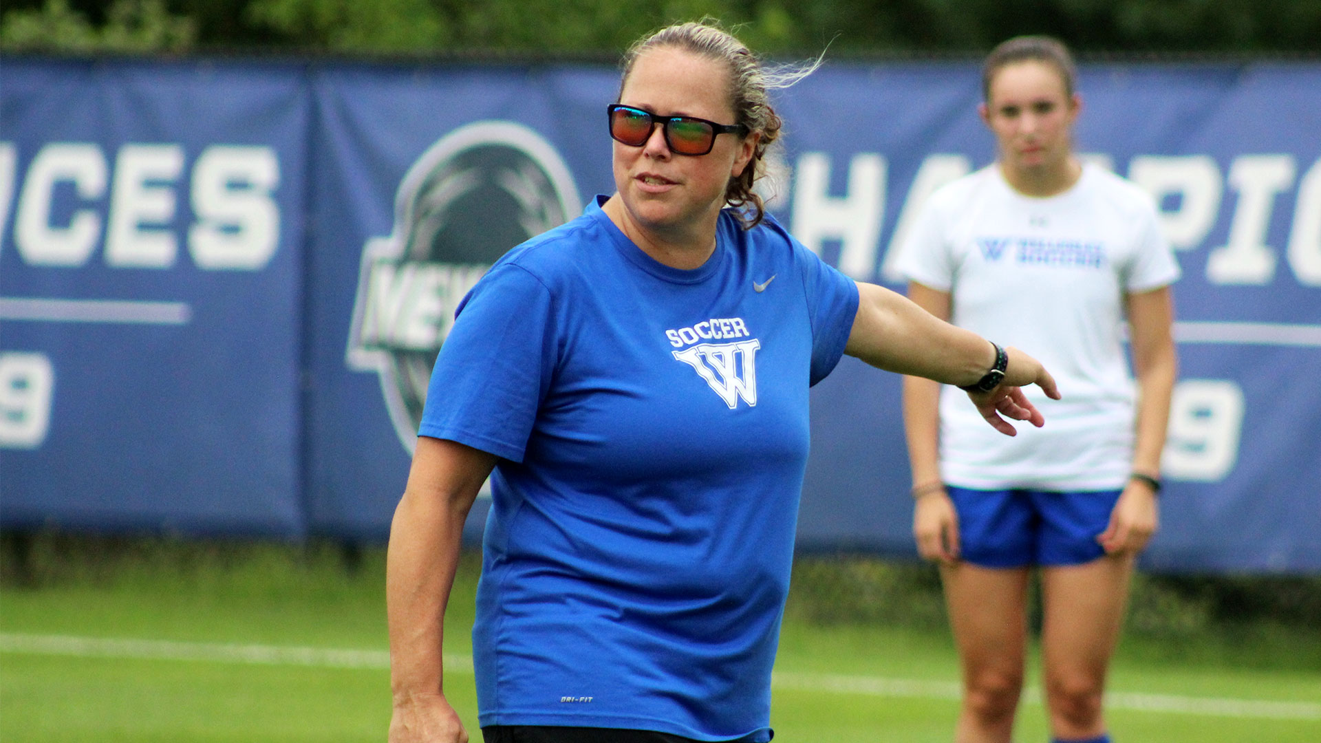 women's soccer coach in blue shirt on grass field directing players